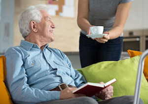 An older adult at home with a book, a cup of tea nearby